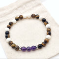 A beaded stretch bracelet made of brown tiger's eye, cream jasper beads, and purple amethyst beads, displayed on a beige canvas drawstring bag.